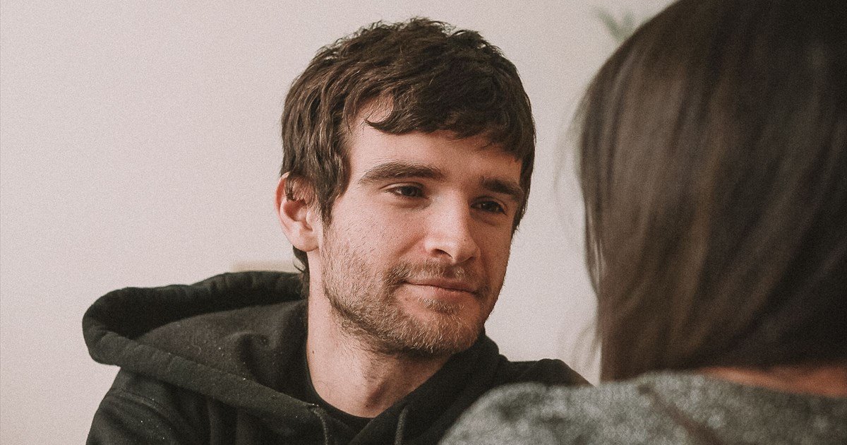 Mann mit lockigem braunem Haar und Bart im dunklen Hoodie im Gespräch mit einer Frau von Angesicht zu Angesicht