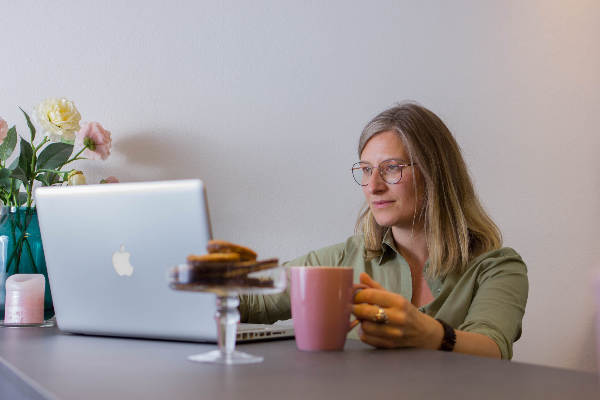 Eine Frau mit Brille sitzt mit einer Kaffeetasse am Laptop und nimmt an einem Online-Webinar teil