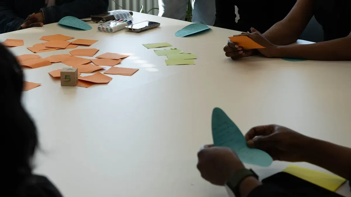 Mehrere Personen sortieren an einem Tisch orange und grüne Zettel