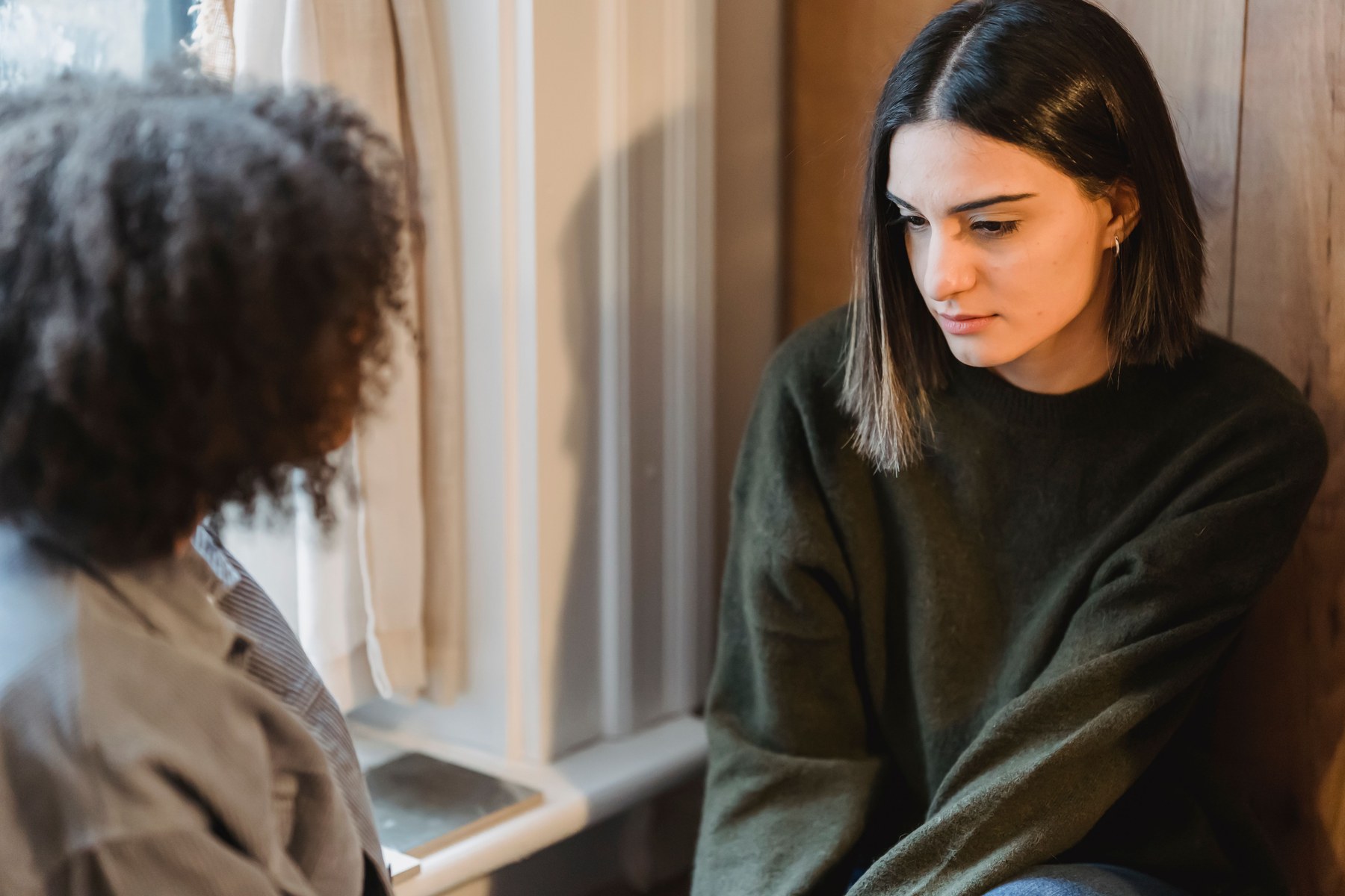 Zwei Frauen sitzen einander am Fenster gegenüber; eine hört der anderen aufmerksam zu.