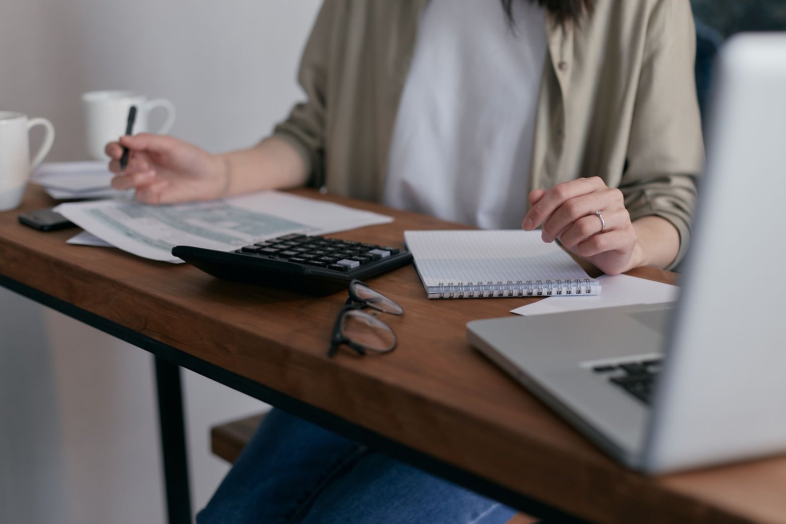 Frau arbeitet am Schreibtisch mit Taschenrechner, Notizbuch und Dokumenten für Finanzplanung.