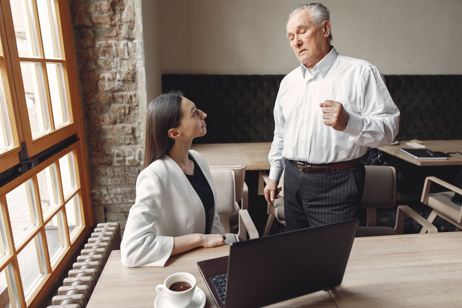Geschäftsmann und Frau im Büro diskutieren vor Laptop und Kaffeetasse am Schreibtisch.