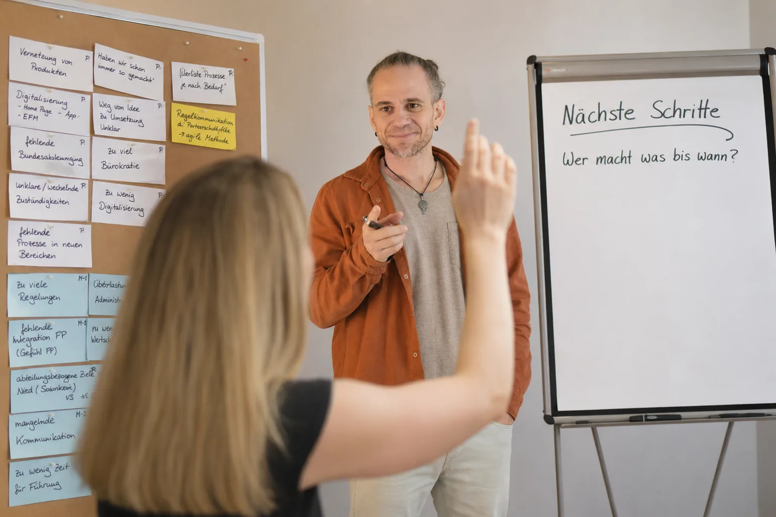Illustration: Moderator vor Pinnwand und Flipchart, eine Person meldet sich