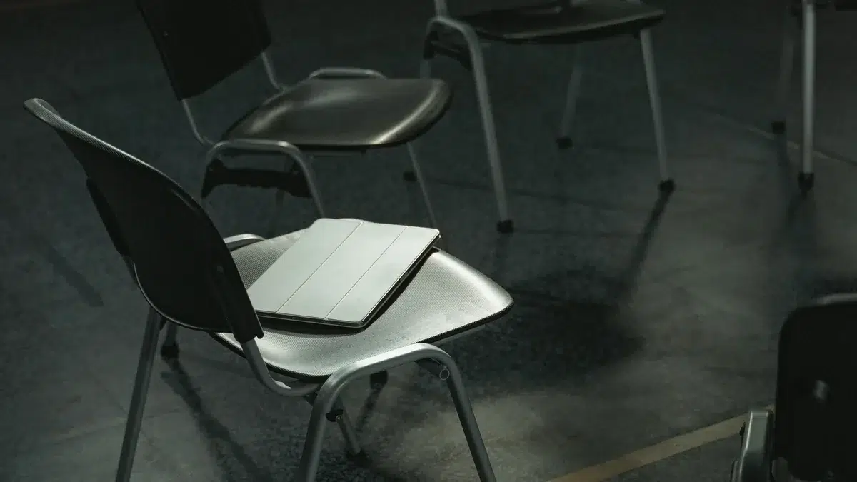 Ein geschlossener Laptop liegt auf einem leeren Stuhl in einem dunklen Besprechungsraum.