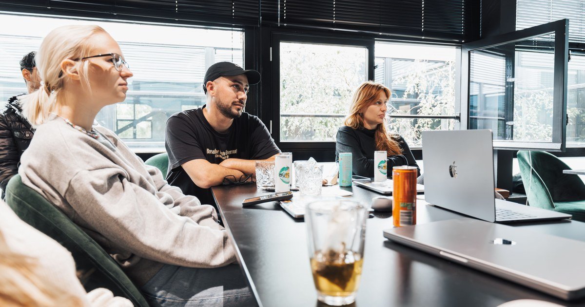 Team im Meetingraum sitzt am Tisch mit Laptops, Getränken und Notizen und diskutiert konzentriert ein Projekt.