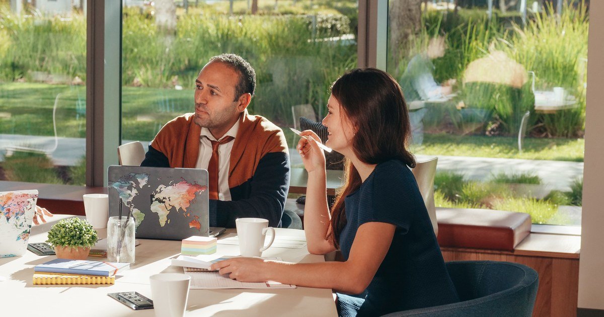 Mann und Frau im Meeting am Tisch mit Laptop, Kaffeetassen und Notizen, Büro mit Gartenblick im Hintergrund