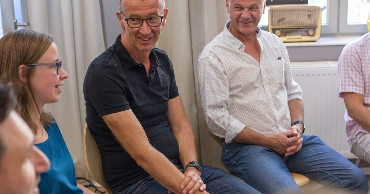 Teilnehmende sitzen im Halbkreis im Seminarraum und lachen miteinander.