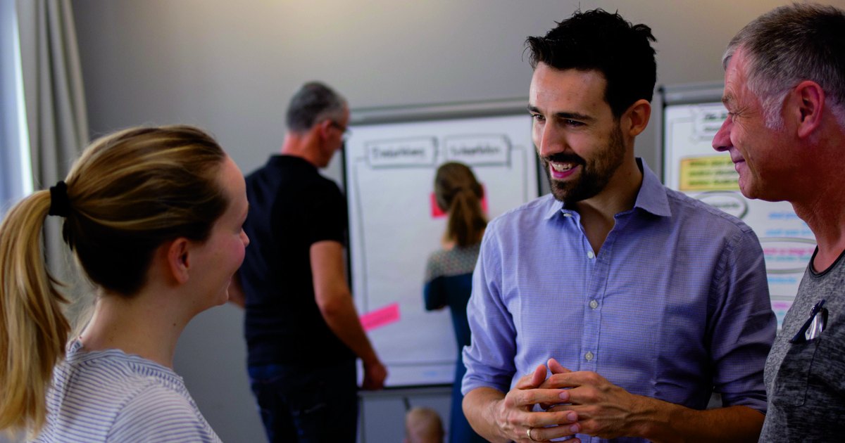 Eine Frau und ein Mann im Gespräch im Seminarraum, beide lächeln, im Hintergrund Flipcharts.