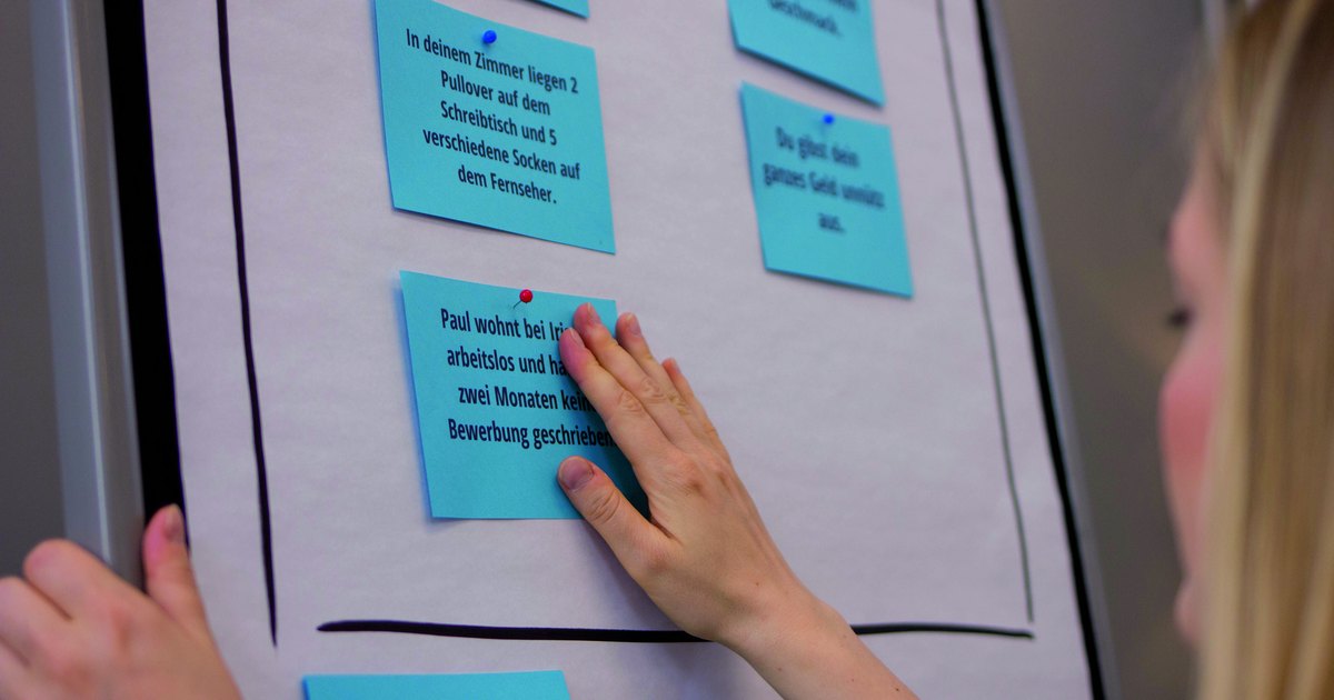 Eine Hand heftet blaue Karten an ein Flipchart, unten steht der Satz Du kommst immer zu spät.