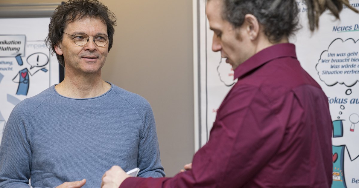 Zwei Männer diskutieren vor einem Flipchart mit der Überschrift Ein neuer Fokus, einer hält Blätter in der Hand.