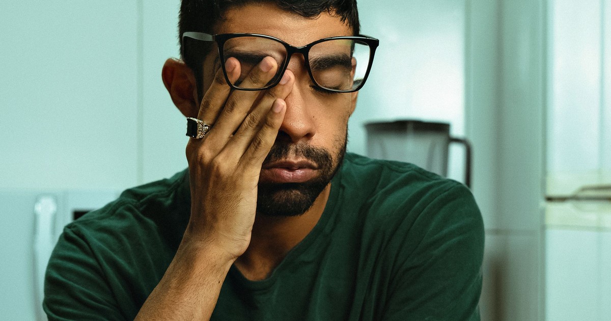 Mann mit Brille sitzt am Küchentisch und reibt sich mit der Hand das Auge.